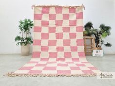 a pink and white checkered blanket sitting on top of a floor next to potted plants