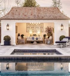 an outdoor living area next to a swimming pool with chairs and tables around it, in front of a white brick house