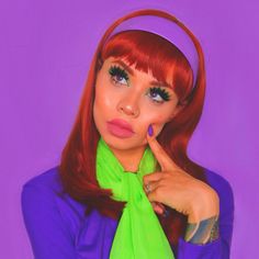 a woman with long red hair wearing a green scarf and purple shirt is posing for the camera