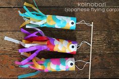 three colorful paper fish on top of a wooden table next to a toothpick