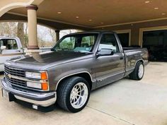 a silver truck parked in front of a garage with two other trucks behind it on the driveway