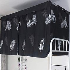 a bed with a black and white leaf print curtain hanging over it's headboard