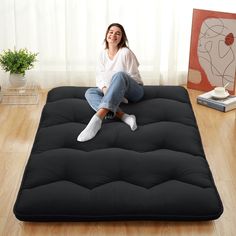 a woman sitting on top of a futon mattress in the middle of a room