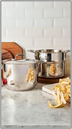 two pots and one pan on a counter with some pasta in it next to other cooking utensils