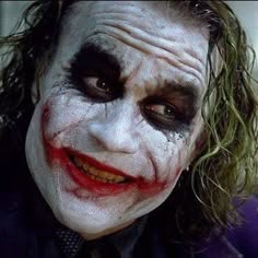 the joker with his face painted in white and black, is looking at the camera