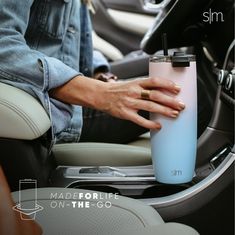 a woman holding a blue cup in her hand while sitting in the driver's seat