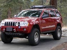 a red jeep parked on the side of a road in front of some pine trees