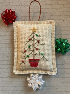 a cross stitch christmas tree ornament hanging on a wall next to two bows