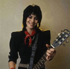 a woman with black hair holding a guitar and wearing a red scarf around her neck