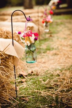 flowers are in mason jars hanging from hay bales on the farm aisle for guests to sit down