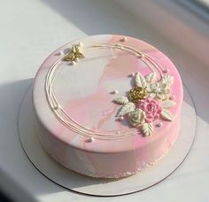 a pink and white cake with flowers on it sitting on top of a table next to a window