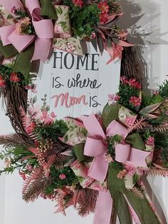 a wreath with pink bows hanging on the wall next to a sign that says home is where mom is