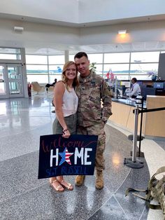 a man and woman holding a welcome home sign in an air force one terminal lobby