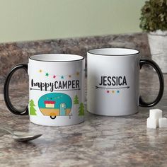 two coffee mugs with the words happy camper and jesus on them sitting on a counter