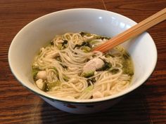 a white bowl filled with noodles and vegetables next to chopsticks on a wooden table