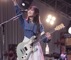 a woman holding a guitar while standing in front of a microphone