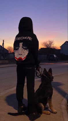 a person standing next to a dog on a sidewalk at sunset with the sky in the background