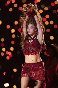 a woman in a red outfit on stage with lights behind her and hands up above her head