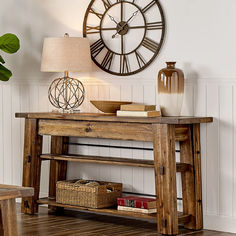 a wooden table with a clock on the wall above it and a lamp next to it