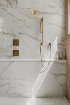 a bathroom with white marble walls and flooring, gold faucet shower head