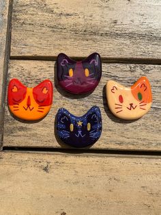 four ceramic cat magnets sitting on top of a wooden bench next to each other