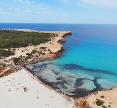 an aerial view of a sandy beach with blue water and green trees in the background