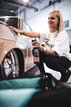 a woman sitting on the ground next to a car holding a beer in her hand