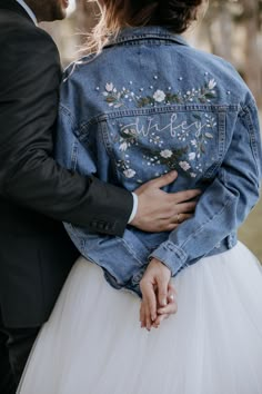 a man in a suit and tie hugging a woman wearing a denim jacket with embroidered words on it