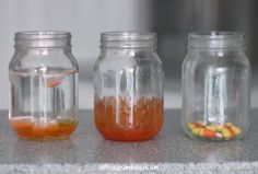 three jars filled with liquid sitting on top of a counter next to candy corn kernels