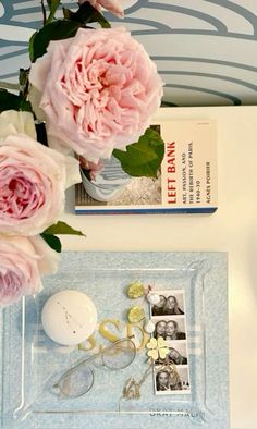 pink flowers are sitting on a tray next to an eyeglass case and other items