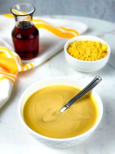 two bowls filled with yellow liquid next to some spoons and a bottle of mustard