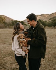 a man and woman holding two puppies in their arms while looking at each other