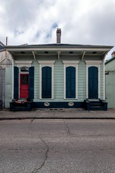 a small blue and white building with shutters on the front, next to a red door