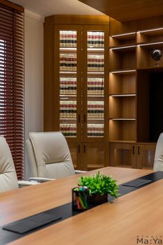 a wooden table with white chairs and a plant on it in front of some bookshelves