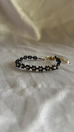 a black beaded bracelet sitting on top of a white bed sheet with gold accents