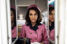 a woman in a pink suit and hat looking at herself in the mirror