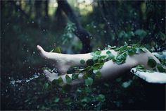 a person laying on their back in the rain with leaves all over her body and feet