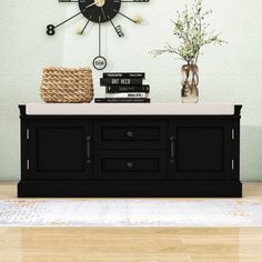 there is a black clock on the wall above a table with books and vases