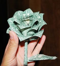 a person holding up a dollar bill origami rose that is folded in half