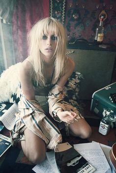 a woman sitting on top of a bed next to an old fashioned guitar case and other items