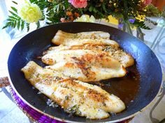 two pieces of fish are cooking in a frying pan on a table next to flowers