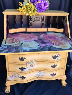 an old dresser has flowers on it and is painted yellow with blue, purple, and pink