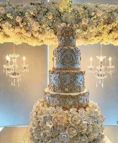 a four tiered wedding cake with white flowers on the bottom and gold trimmings