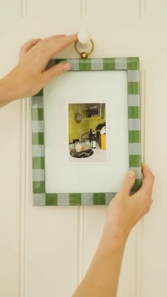 a person is holding up a green and white frame with a picture on the wall