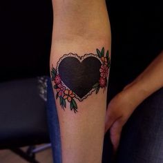 a heart tattoo with flowers around it on the forearm and hand, in front of a woman's arm