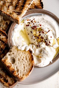 a plate topped with bread and cream on top of a white table next to slices of toast