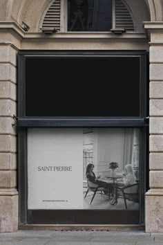 an advertisement is displayed in the window of a store on a city street with people sitting at a table