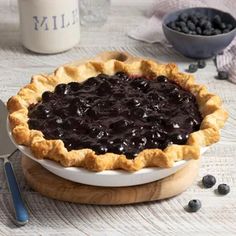 a blueberry pie sitting on top of a white plate next to a bowl of blueberries