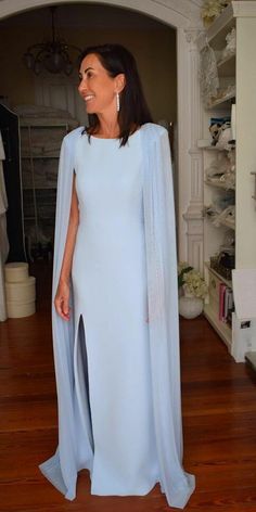 a woman wearing a blue dress and cape standing in a room with hardwood floors, looking off to the side