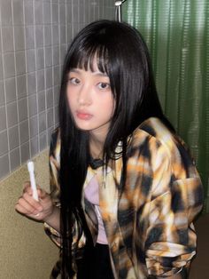 a girl with long black hair holding a toothbrush in her hand and looking at the camera